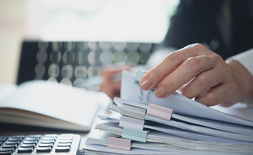 Eine Geschäftsfrau arbeitet an einem Schreibtisch mit einem Stapel Papierakten, um Unternehmensdokumente zu prüfen und zu organisieren.