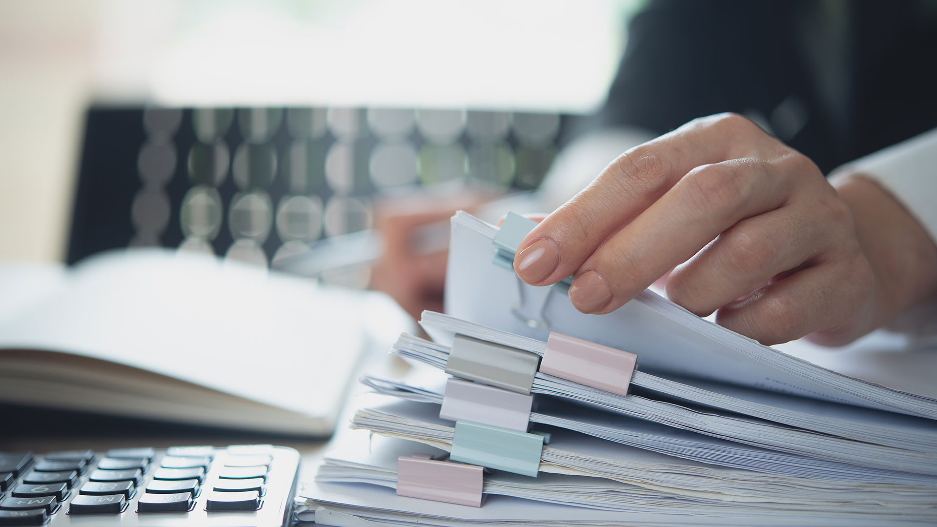 Eine Geschäftsfrau arbeitet mit einem Stapel Papierakten und überprüft Unternehmensdokumente auf einem Bürotisch.