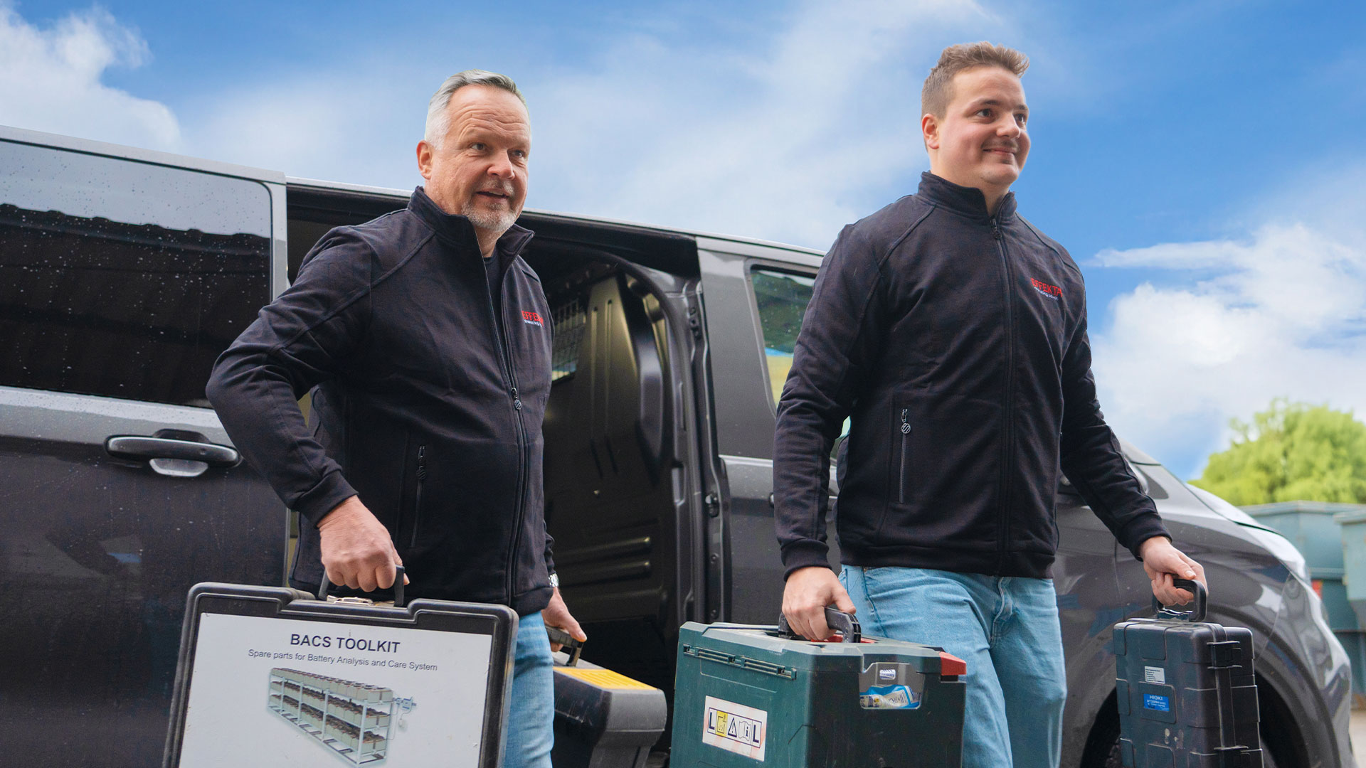 Zwei EFFEKTA-Mitarbeiter holen Werkzeugkoffer und Material aus einem Transporter, um Wartungsarbeiten an einer USV-Anlage durchzuführen.