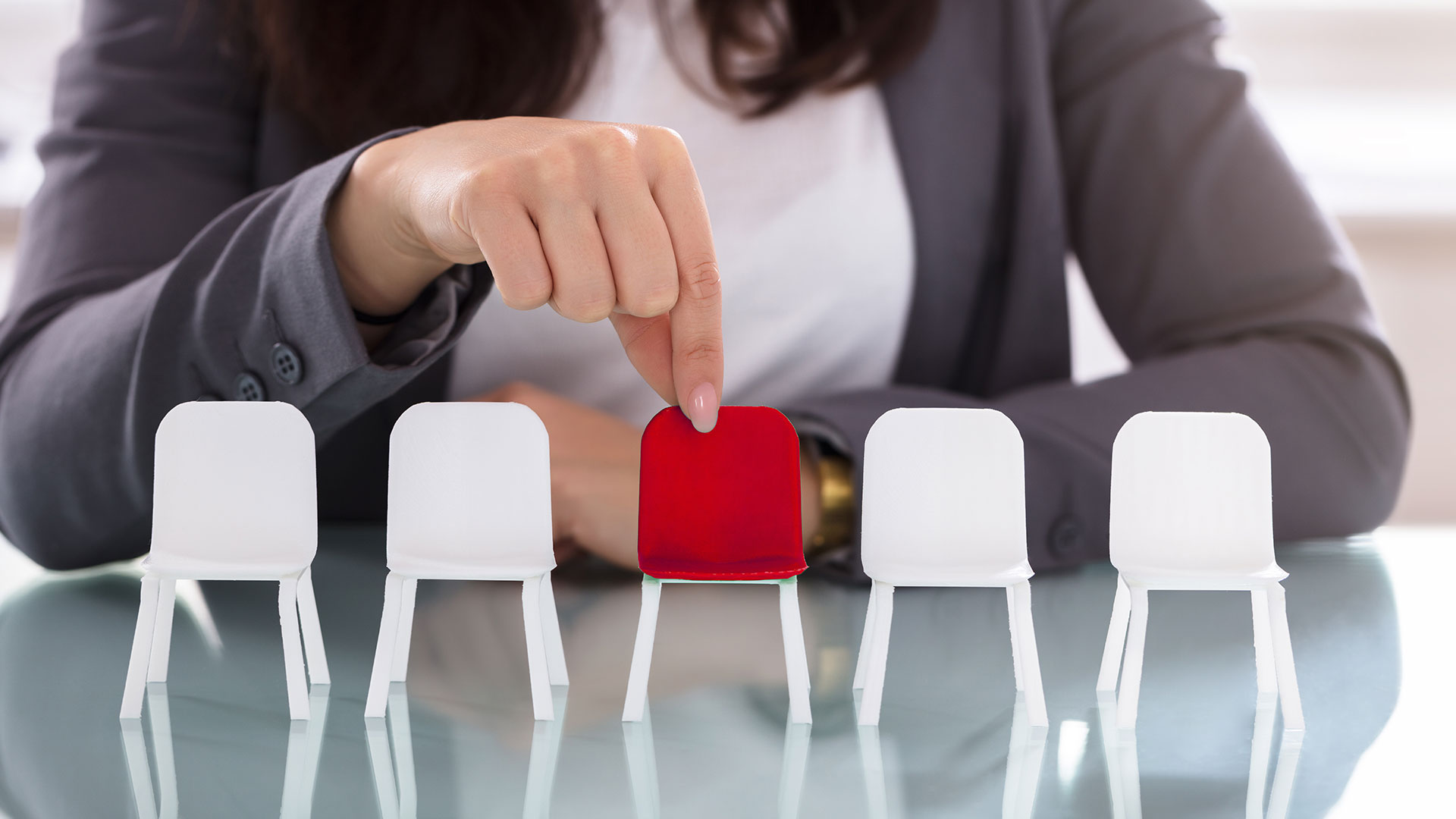 Geschäftsfrau wählt einen roten Stuhl aus einer Reihe weißer Stühle, symbolisch für die Wahl des richtigen Arbeitsplatzes.
